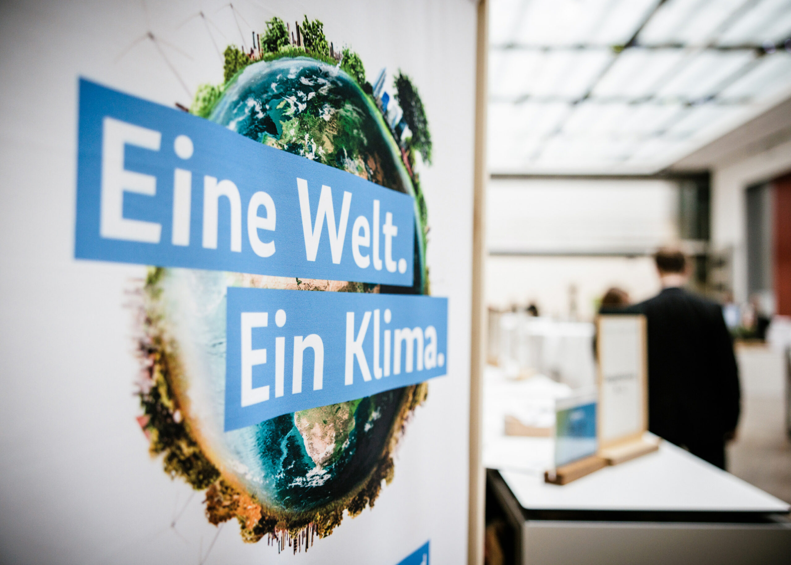 Ein Platkat mit der Aufschrift 'Eine Welt. Ein Klima.' steht in einem Messeraum